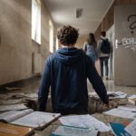 Ein Teenager bricht in einem düsteren Schulflur durch den maroden Boden, während Mitschüler vorbeigehen. Im Hintergrund hängt eine Wanduhr und an der Tür steht ein Fragezeichen. Symbolisiert das Durchrutschen im deutschen Bildungssystem.